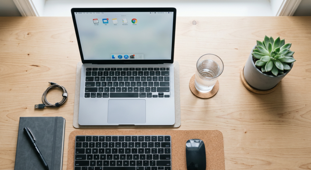 A clean, top-down professional workspace featuring a modern laptop, a glass of water, and a succulen